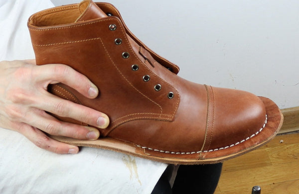 Brown leather boot held by a hand against a white background