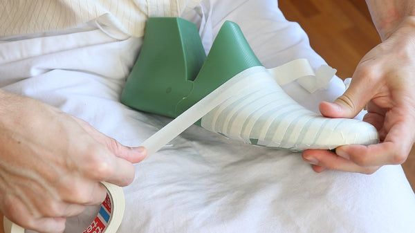 Person applying tape to a green shoe last