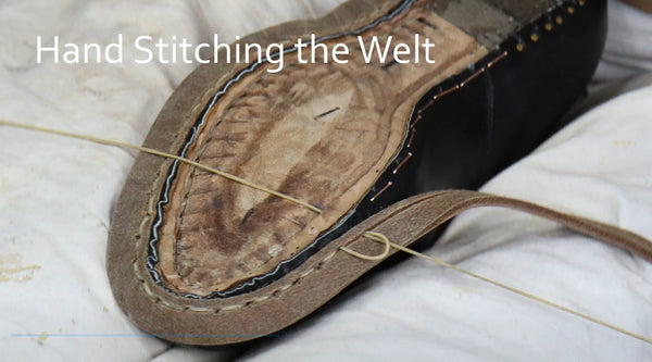 A close-up of a hand stitching the welt of a brown leather shoe on a white fabric background, with the text 'Hand Stitching the Welt' overlaid at the top.