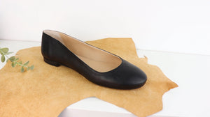 ballet pumps shoe made of black goat skin leather, placed on a piece of brown cow leather