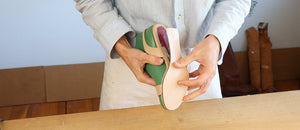 Shoemaker demonstrating how to attach the sole to a leather shoe on a green last during the shoemaking process.