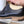 A close-up of a black leather dress shoe with a wooden shoe tree inserted, held by a hand in a workshop setting.