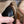 A close-up of a person's hands holding a black leather shoe or boot while using a wooden and metal tool to shape or polish the edge of the leather.