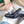 A close-up of a person's hands shining oil onto a black leather dress shoe with a white shoe tree inside, set in a workshop environment.